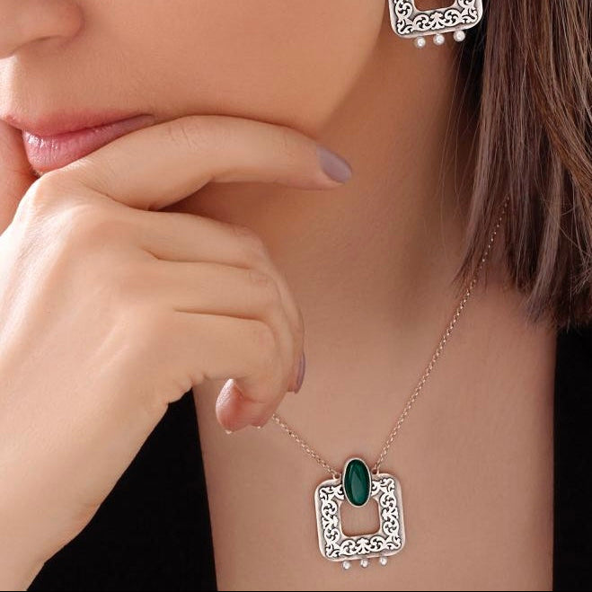 Close-up of a woman wearing  Persian silver earrings and necklace with green gemstones.